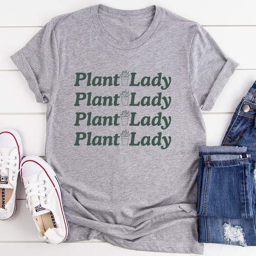 A grey Plant Lady Tee shown sitting on a white deck with a pair of blue jeans next to it and a pair of white tennis shoes