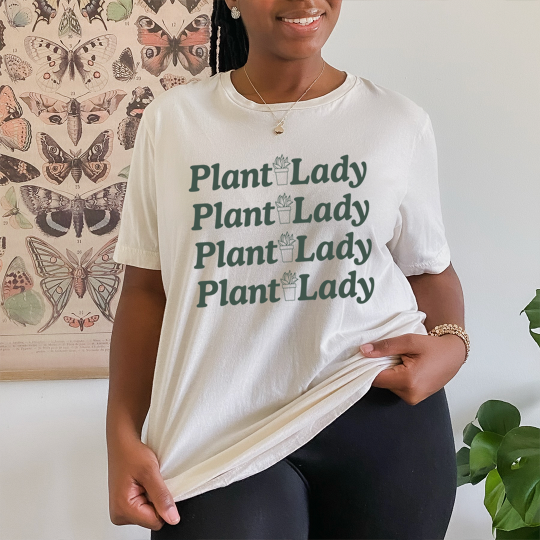 A female model wearing the Plant Lady Tee Shirt is white with the words plant lady repeated 4 times vertically with a plant in the middle words are in green