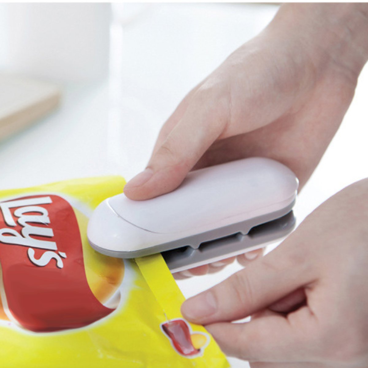 Shows the Snack Bag Open And Seal Mini Machine 2 In 1 being used to seal a bag of potato chips