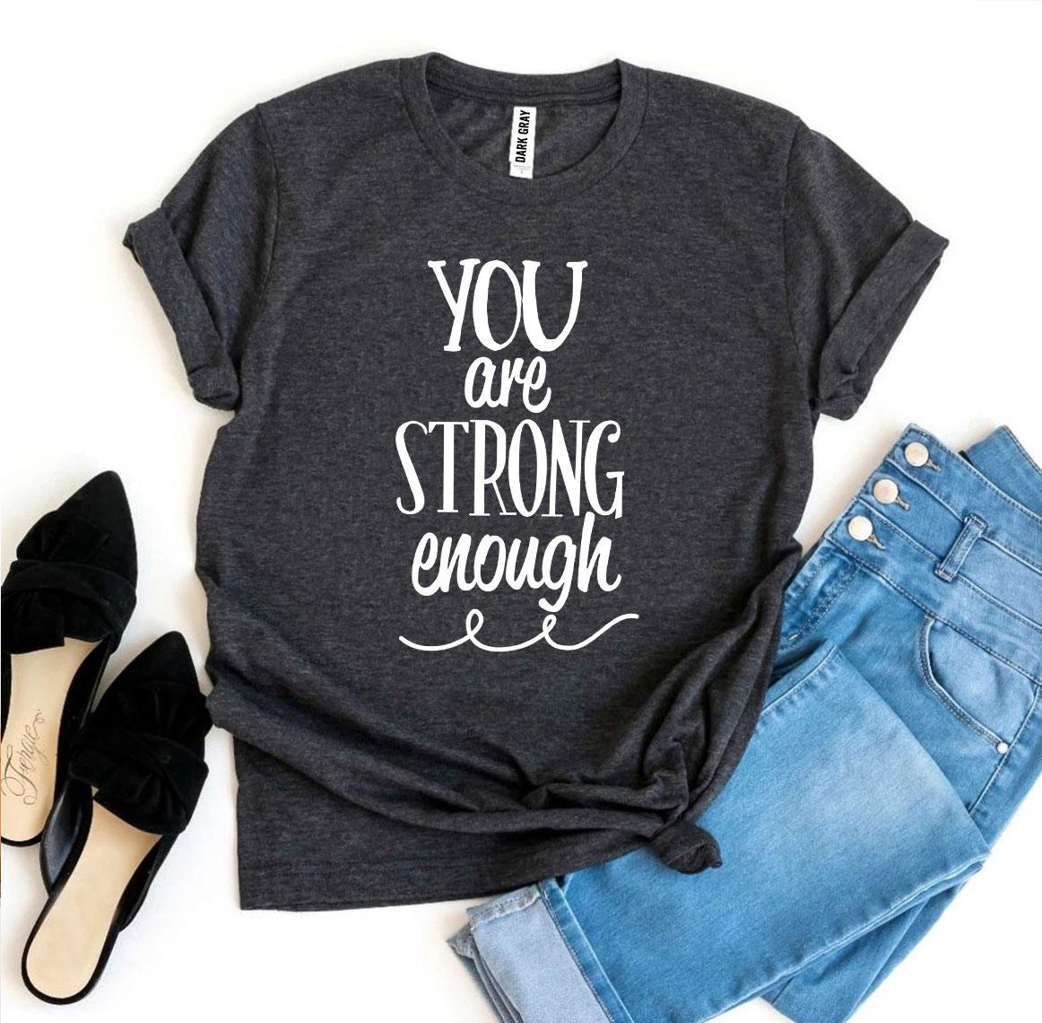 A black and white You Are Strong Enough T-shirt shown with a pair of jeans next to it and a pair of black heels