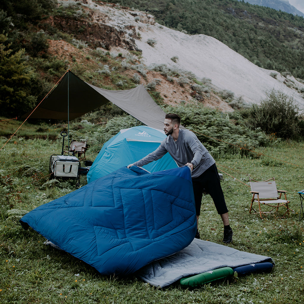 A male model at a campsite shown deploying the Camfy 53/24F Sleeping Bag